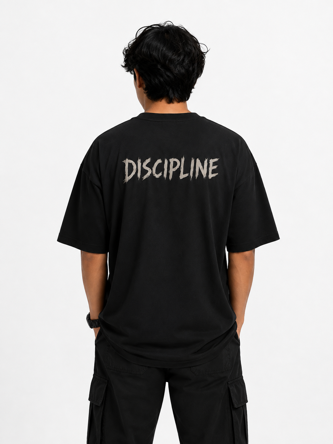 A man viewed from behind wearing a black t-shirt with the word 'DISCIPLINE' printed across the back in a textured light gray font, paired with black cargo pants against a plain white background.